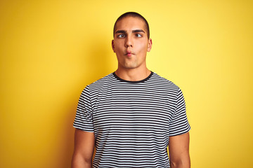 Obraz premium Young handsome man wearing striped t-shirt over yellow isolated background making fish face with lips, crazy and comical gesture. Funny expression.