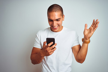 Young handsome man using smartphone over yellow isolated background very happy and excited, winner expression celebrating victory screaming with big smile and raised hands