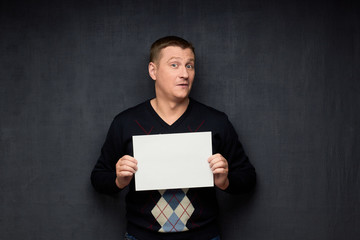Portrait of surprised man holding white blank paper sheet