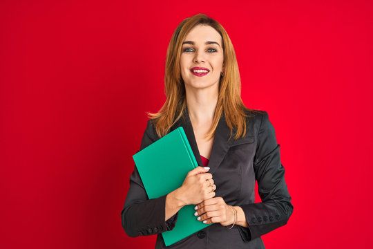 Young beautiful redhead businesswoman wearing suit holding book
