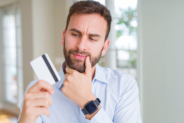 Handsome business man holding credit card serious face thinking about question, very confused idea