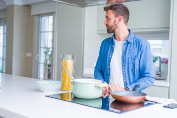 Handsome man cooking italian spaghetti pasta at the kitchen looking to side, relax profile pose with natural face with confident smile.