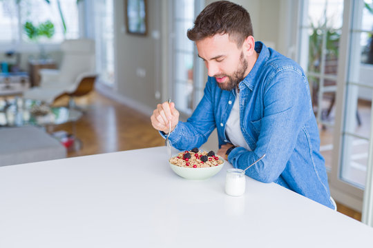 Handsome man having breakfast eating cereals at home and smiling