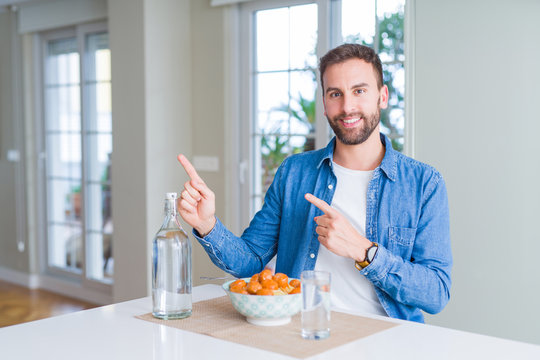 Handsome man eating pasta with meatballs and tomato sauce at home smiling and looking at the camera pointing with two hands and fingers to the side.