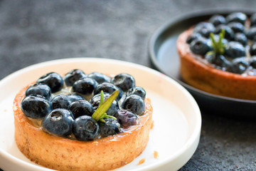 Delicious blueberry tartalets with vanilla cream on black and white plates  on a grey background. Top view.