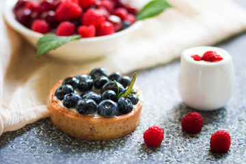 Tartalets with blueberry berries, plate with fresh raspberry and dairy with sour cream on the grey surface. 
