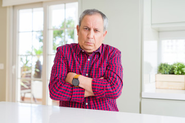 Handsome senior man at home skeptic and nervous, disapproving expression on face with crossed arms. Negative person.