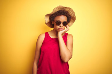 African american woman wearing summer hat and sunglasses over yellow isolated background thinking looking tired and bored with depression problems with crossed arms.