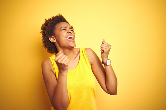 Beauitul african american woman wearing summer t-shirt over isolated yellow background very happy and excited doing winner gesture with arms raised, smiling and screaming for success. 