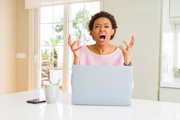 Young african american woman working using computer laptop crazy and mad shouting and yelling with...