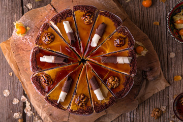 Caramel cake with nuts and chocolate, cut into slices on a rustic background. View from above. Free space for text.
