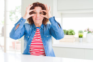 Middle age senior woman with curly hair wearing denim jacket at home Trying to open eyes with...