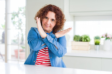 Middle age senior woman with curly hair wearing denim jacket at home Rejection expression crossing arms doing negative sign, angry face