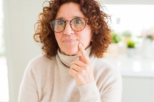 Beautiful senior woman wearing turtleneck sweater and glasses with hand on chin thinking about question, pensive expression. Smiling with thoughtful face. Doubt concept.