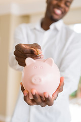 Handsome young african man putting a coin inside piggy bank smiling, excited about investment