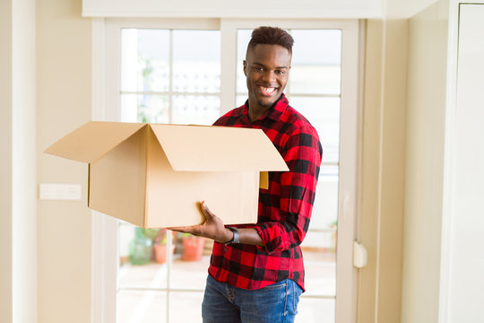 Young African American Man Holding A Carton Box, Packing Cardboard Delivery Package At Home