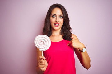 Young beautiful woman eating sweet candy over pink isolated background with surprise face pointing finger to himself