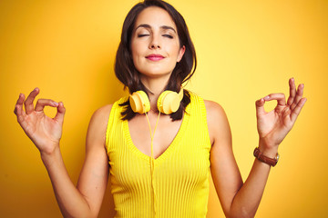 Young beautiful woman wearing headphones over yellow isolated background relax and smiling with eyes closed doing meditation gesture with fingers. Yoga concept.