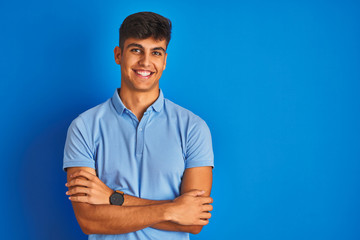 Young indian man wearing casual polo standing over isolated blue background happy face smiling with...