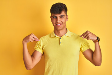 Young indian man wearing casual polo standing over isolated yellow background looking confident with smile on face, pointing oneself with fingers proud and happy.