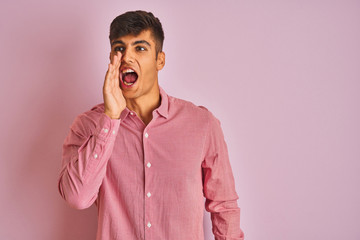 Young indian man wearing elegant shirt standing over isolated pink background shouting and screaming loud to side with hand on mouth. Communication concept.