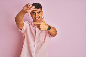 Young indian man wearing casual shirt standing over isolated pink background smiling making frame with hands and fingers with happy face. Creativity and photography concept.