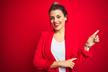 Young beautiful business woman standing over red isolated background with a big smile on face, pointing with hand finger to the side looking at the camera.