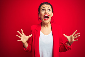 Young beautiful business woman standing over red isolated background crazy and mad shouting and yelling with aggressive expression and arms raised. Frustration concept.