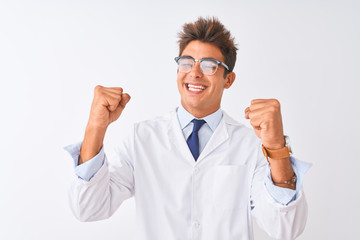 Young handsome sciencist man wearing glasses and coat over isolated white background very happy and excited doing winner gesture with arms raised, smiling and screaming for success. 