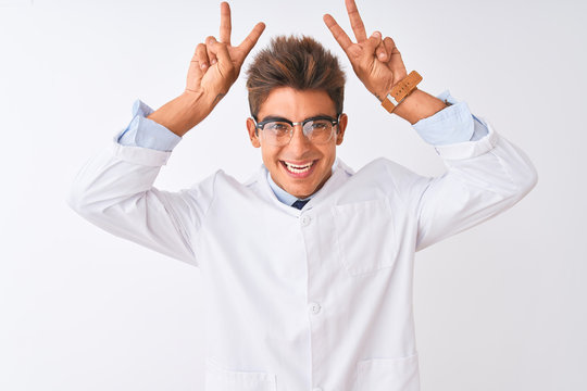 Young handsome sciencist man wearing glasses and coat over isolated white background Posing funny and crazy with fingers on head as bunny ears, smiling cheerful