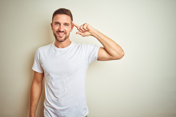 Young handsome man wearing casual white t-shirt over isolated background Smiling pointing to head...