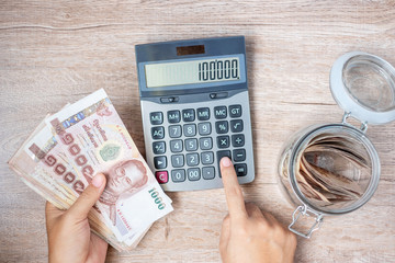 Businessman hand holding Thai Baht banknote stack and using calculator. business, accounting, money, investment , finance and payment concepts