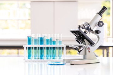 Closed up microscope with tube and glass in laboratory. Blue chemist in glass tubes on lab white table.