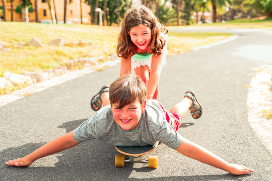 Sister and brother playing with longboard in the park. Young people happy in a perfect summer. Holiday, sport and younger concept. Focus on the boy - Image.