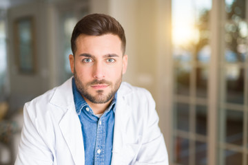 Young handsome doctor man at the clinic with serious expression on face. Simple and natural looking...