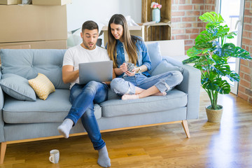 Fototapeta premium Young couple moving to a new home relaxing sitting on the sofa using computer laptop, smiling happy for moving to new apartment