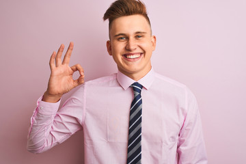 Young handsome businessman wearing shirt and tie standing over isolated pink background smiling positive doing ok sign with hand and fingers. Successful expression.