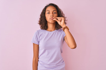 Young brazilian woman wearing t-shirt standing over isolated pink background mouth and lips shut as zip with fingers. Secret and silent, taboo talking