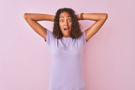 Young brazilian woman wearing t-shirt standing over isolated pink background Crazy and scared with hands on head, afraid and surprised of shock with open mouth