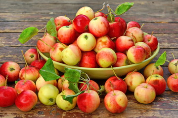 red yellow apples with green foliage in a deep bowl and scattered around it on old wooden plank surface