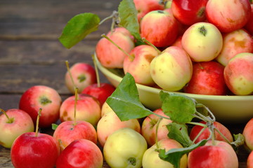 Left part deep bowl with red yellow apples with green foliage and scattered apples around it on old wooden plank surface. Closeup