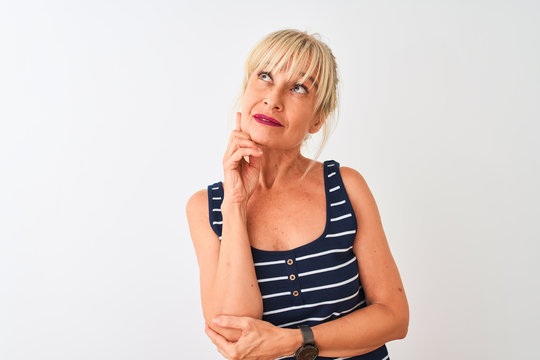Middle age woman wearing casual striped t-shirt standing over isolated white background with hand on chin thinking about question, pensive expression. Smiling with thoughtful face. Doubt concept.