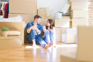 Young beautiful couple relaxing sitting on the floor around cardboard boxes at home, smiling happy moving to a new house