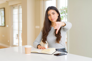 Young woman reading a book and drinking a coffe with angry face, negative sign showing dislike with thumbs down, rejection concept