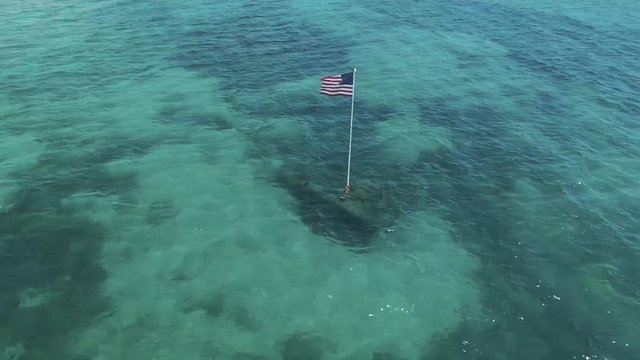 American Flag on Ocean Water. Aerial Circle of United States flagship on crystal clear water, blow in the wind.