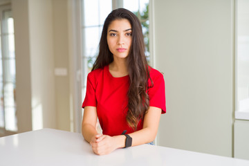 Young beautiful woman at home on white table with serious expression on face. Simple and natural looking at the camera.