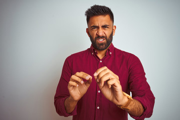 Young indian man wearing red elegant shirt standing over isolated grey background disgusted...