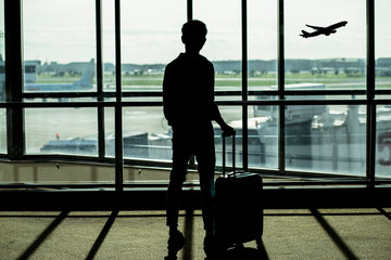 silhouette of man standing with luggage at terminal in airport for waiting flight to travel