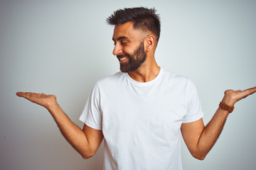 Young indian man wearing t-shirt standing over isolated white background smiling showing both hands...