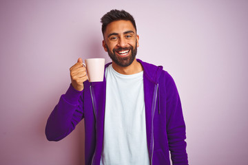 Indian man wearing purple sweatshirt drinking cup of coffee over isolated pink background with a happy face standing and smiling with a confident smile showing teeth